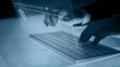 Hände tippen auf Tastatur mit Hologramm von Sicherheits- und Digitalisierungsfunktionen.