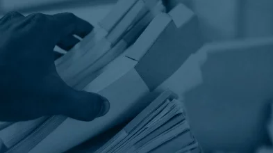 Hand hält Stapel papierbasierter Dokumente zur professionellen Digitalisierung von Akten und Archiven.